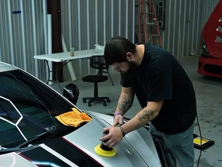 A Cloak detailer machine-polishing the hood of a silver Corvette Z06.