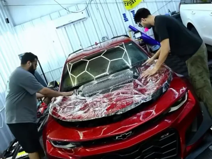 Two Cloak installers laying wet paint protection film over the hood of a red Camaro ZL1 1LE.