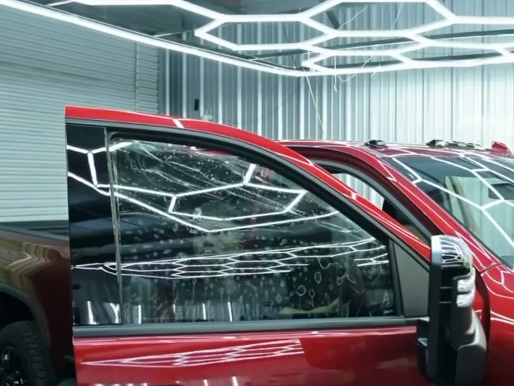 The open driver's door of a red Chevrolet Silverado HD in the showroom, the glass still clear enough to see the lights through it.